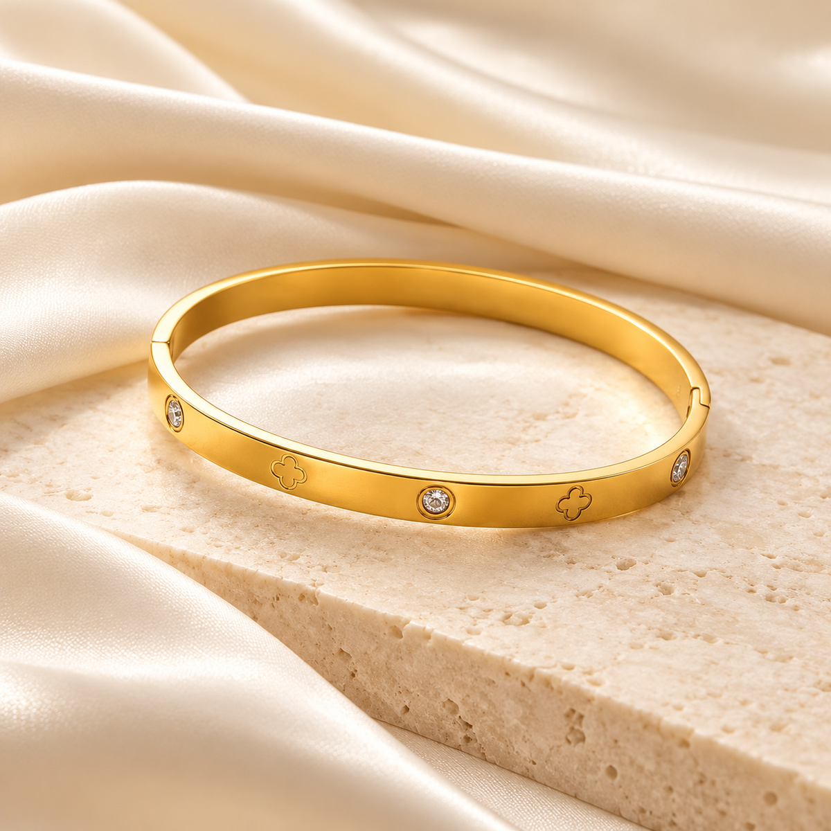 Bracelet jonc Céliane doré, trèfles gravés et détails scintillants sur fond ivoire