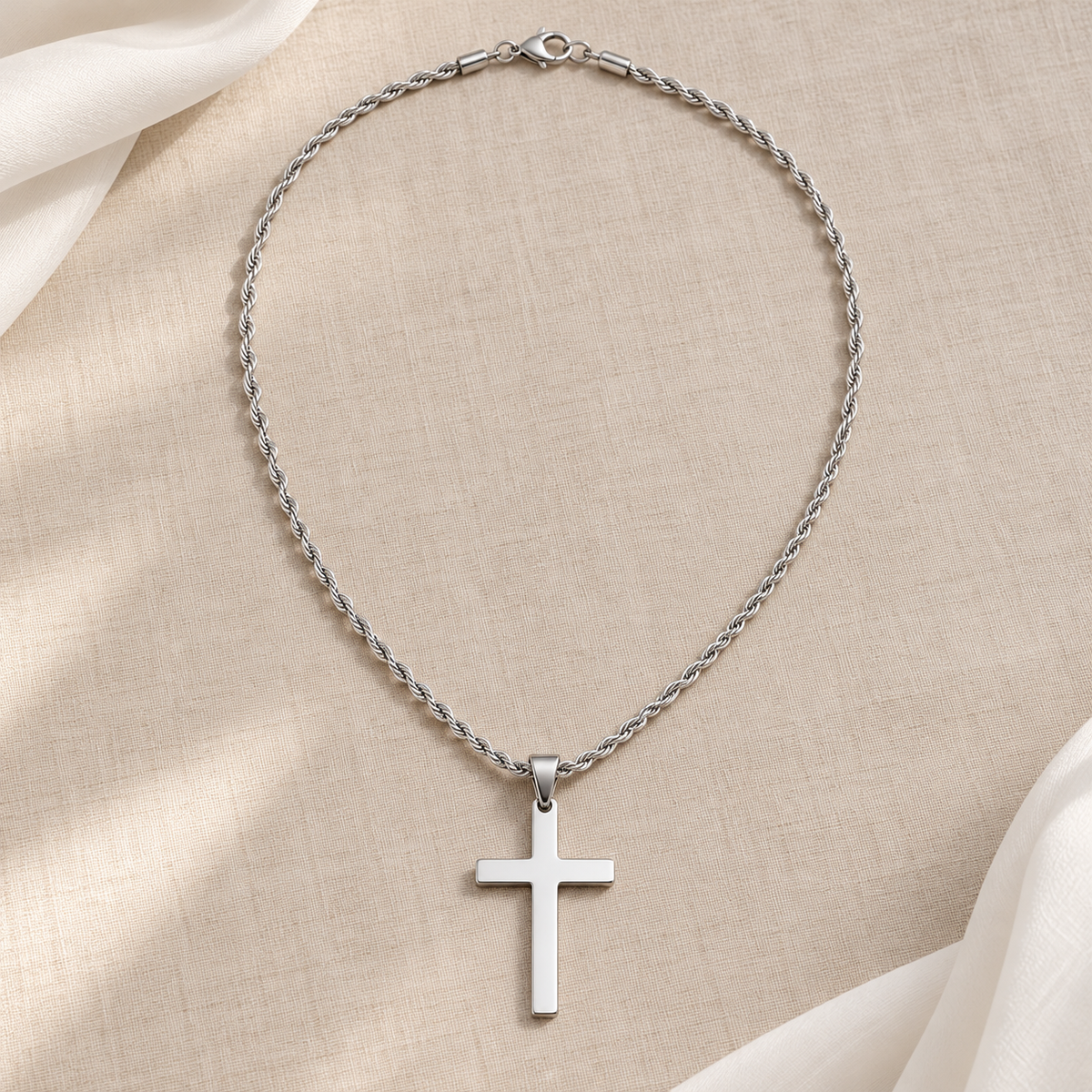 Collier Gabriel croix argentée — vue à plat sur lin beige
